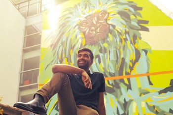 Man Wearing Blue Polo Shirt Sitting Besides Lion Painting