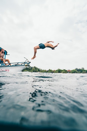 Man Wearing Blue Shorts Performing Back Flip over Body of Water