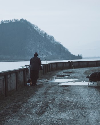 Man Wearing Brown Coat Near a Body of Water With Fishing Rods at Daytime