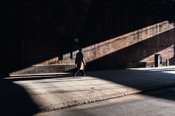 man wearing brown coat walking on grey concrete road near brown wall