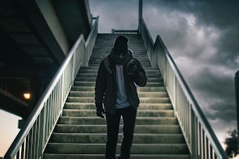 man wearing brown jacket walking on the stair under black sky