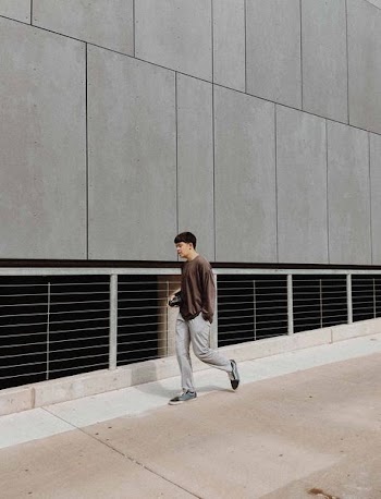 man wearing brown shirt standing near gray wall during daytime