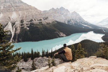 Man Wearing Brown Vest Sitting on Mountain Looking at Lake