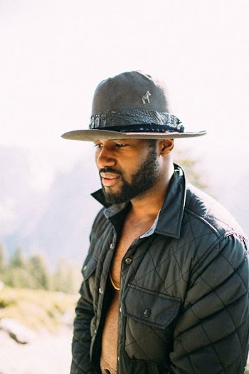 man wearing cowboy hat and buffer jacket looking down outdoor