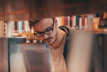 Man Wearing Eyeglasses and Hoodie Inside Library
