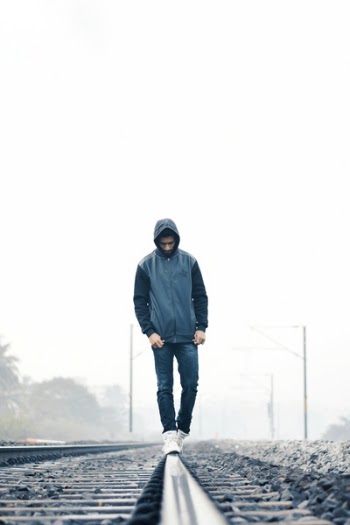 Man Wearing Gray and Black Zip-up Hoodie With Black Denim Jeans and White Shoes Walking on Train Railing Behind White Fog