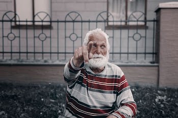 man wearing gray and red striped long-sleeved shirt sitting near gray metal fence