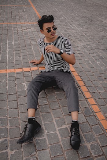 Man Wearing Gray and White Striped Crew-neck T-shirt and Gray Pants Sitting on Concrete Pavement