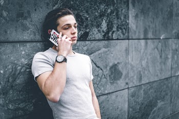 Man Wearing Gray Crew-neck T-shirt Leaning on Gray Wall