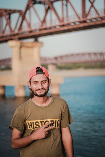 Man Wearing Gray Historic-printed T-shirt and Red Snapback Cap Taking Photo Beside Body of Water