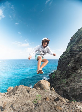 Man Wearing Gray Hoodie Jumping at Rock