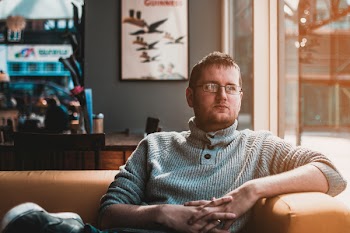 Man Wearing Gray Knitted Sweater Sitting on Brown Fabric Sofa