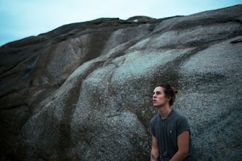 man wearing gray shirt leaning on rock