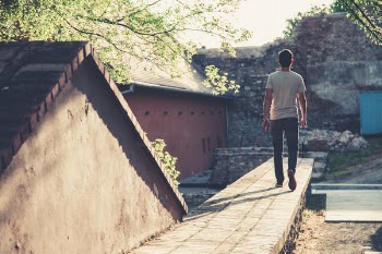 Man Wearing Gray T-shirt and Black Denim Jeans Walking Towards Gray Concrete Pathway