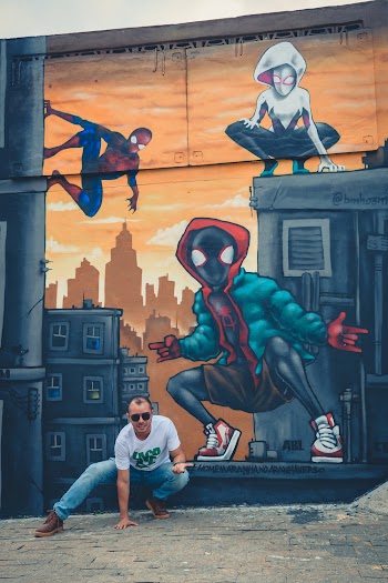 Man Wearing Green and White Crew-neck Shirt Squatting In front of Wall with graffiti 