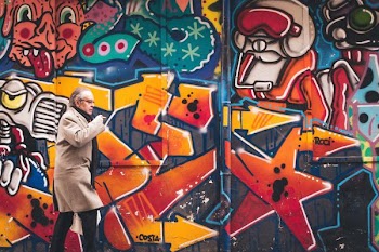 man wearing grey coat walking beside wall with graffiti