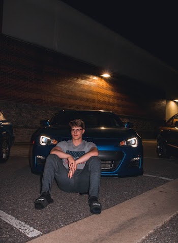 Man Wearing Grey Crew-neck Shirt And Grey Track Pants Sitting In Front Of Blue Vehicle