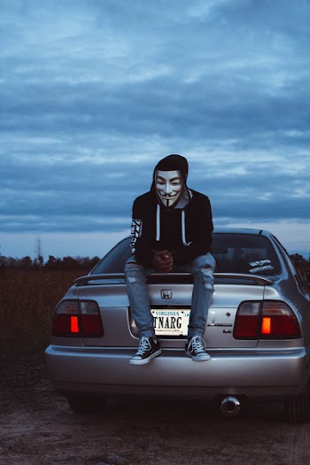 Man Wearing Guy Fawkes Mask Sitting on Gray Honda Vehicle