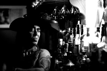 man wearing hat beside bottles on grayscale photography
