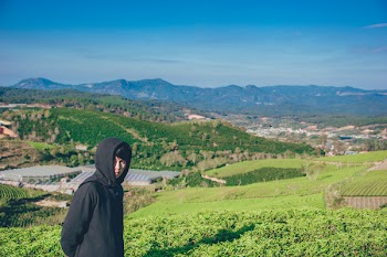 Man Wearing Hoodie Taking Picture With Mountain and Field Photography