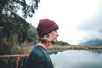 man wearing maroon knit hat standing in front of body of water during daytime