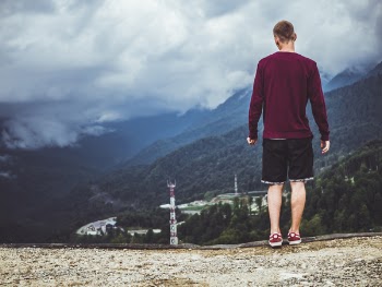 Man Wearing Maroon Sweater and Black Shorts Standing in Front of Mountain