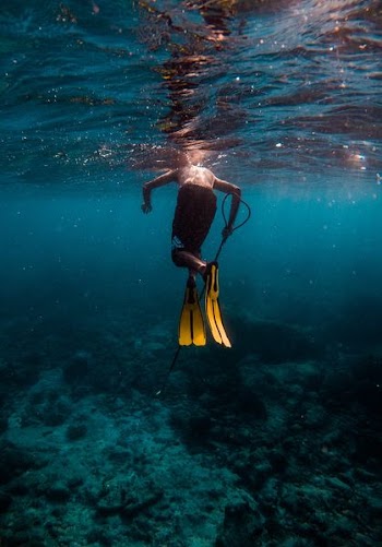 man wearing pair of yellow flippers swimming under water