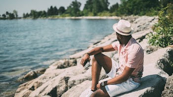 Man Wearing Pink Polo Shirt and White Shorts Sitting on Rock