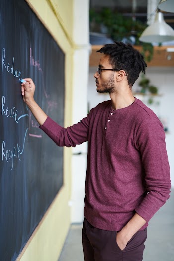 Man Wearing Purple Top and Pants Writing on Chalkboard