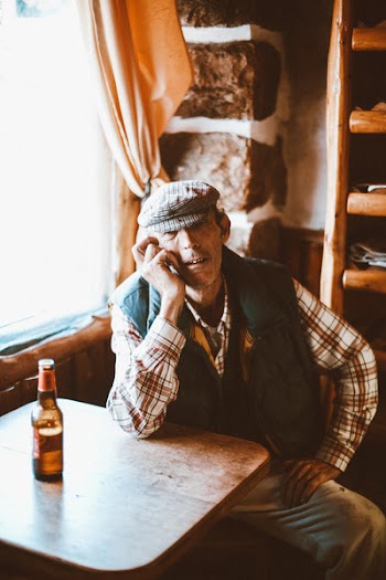 Man Wearing Red and White Plaid Shirt and Black Vest Sitting Beside Brown Wooden Table
