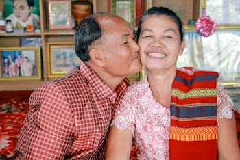 Man Wearing Red and White Plaid Shirt Kissing Woman Wearing White and Red Floral Sari Dress