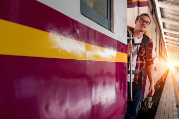 Man Wearing Red Button-up Shirt and Blue Jeans Holding Silver Train Side Rail