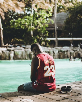 Man Wearing Red Lebron James 23 Jersey Shirt Sitting on Dock Near Body of Water