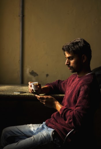 Man Wearing Red Sweater Sitting at Brown Table Holding White Cup