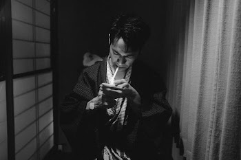 man wearing robe lighting cigarette stick inside room with curtain