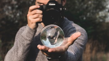 Man Wearing Space-dyed Sweater Holding Water Globe While Holding Black Canon Camera