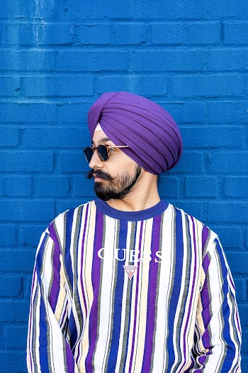 Man Wearing Striped Long-sleeved Crew-neck T-shirt and  Purple Turban Leaning on Blue Wall