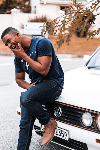 Man Wearing T-shirt and Jeans Sitting on White Volkswagen Car Hood