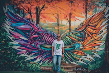 Man Wearing White and Green Crew-neck Shirt Leaning on  Graffiti Wall Art