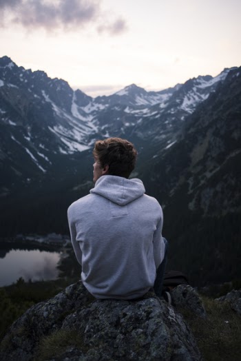 Man Wearing White Hoodie Sitting on a Rock With a View on Mountain