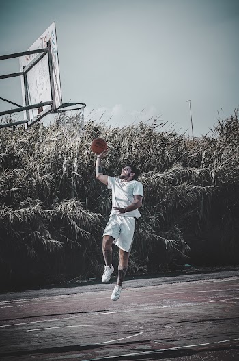 Man Wearing White Shirt Jumps in Front of Basketball Ring