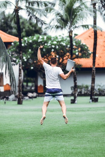 Man Wearing White Shirt Wearing Black Shorts Hopping on Green Grass