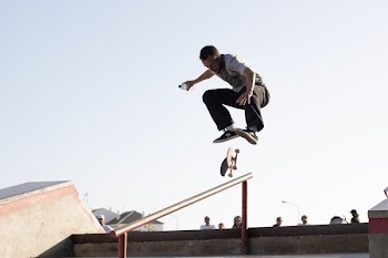 Man Wearing White T-shirt Performing Skateboard Tricks on Rail Under Blue Sky
