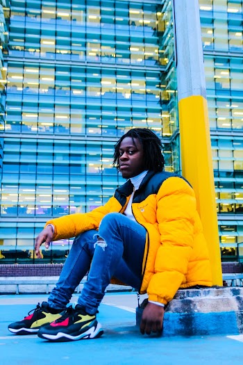 Man Wearing Yellow And Black Zip-up Bubble Jacket Sitting Beside Metal Post