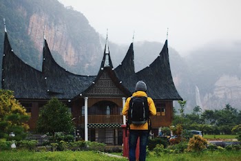 Man Wearing Yellow Jacket and Carrying Backpack Facing Black Roof House