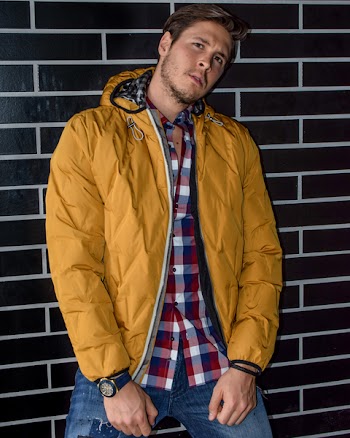 Man Wearing Yellow Zip-up Jacket Leaning on Brown Brick Wall