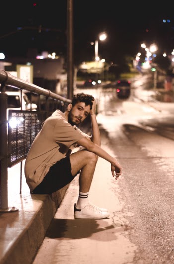Man Wears Brown Shirt and Black Shorts Seats Beside Black Street Post