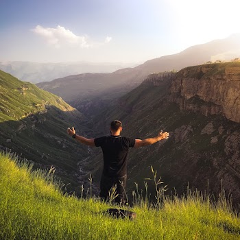 Man With Arms Spread Out While Standing On Green Grass Mountain