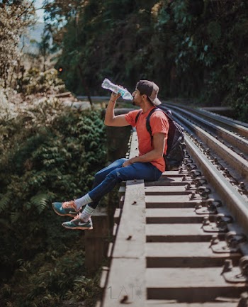 Man With Backpack Sitting  on Railroad and Drinks Water