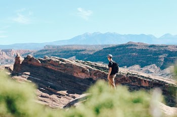 man with backpack standing on gray rocky mountain at daytime